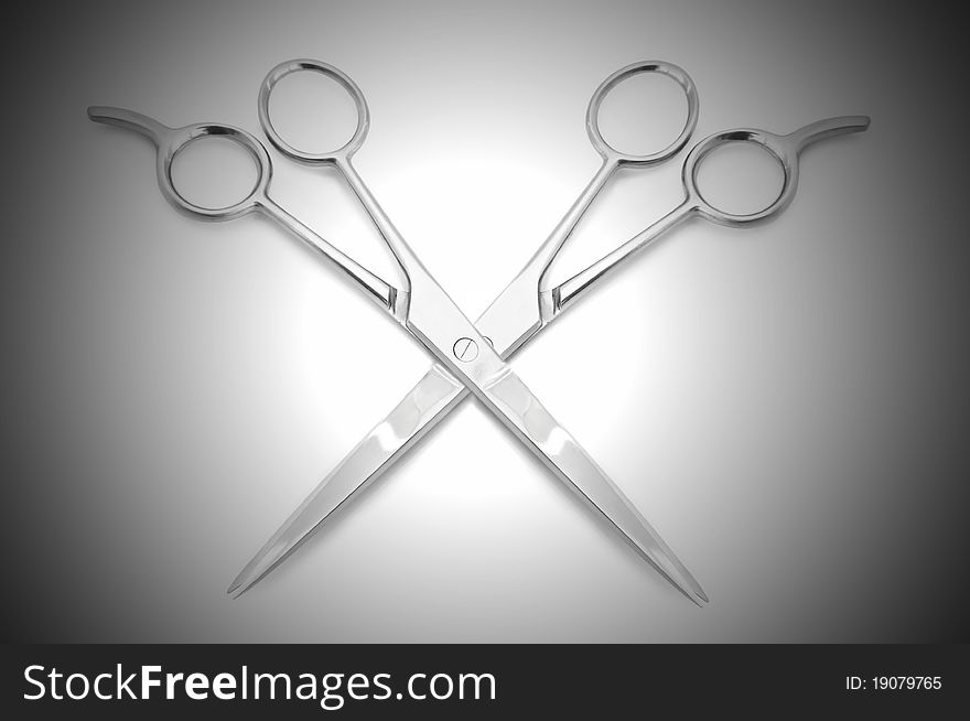 Two stainless steel hairdressing scissors overlapping each other against a white and grey light effect background. Two stainless steel hairdressing scissors overlapping each other against a white and grey light effect background