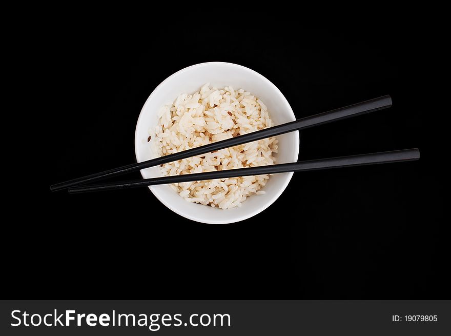 White bowl of rice with chopsticks on the black background