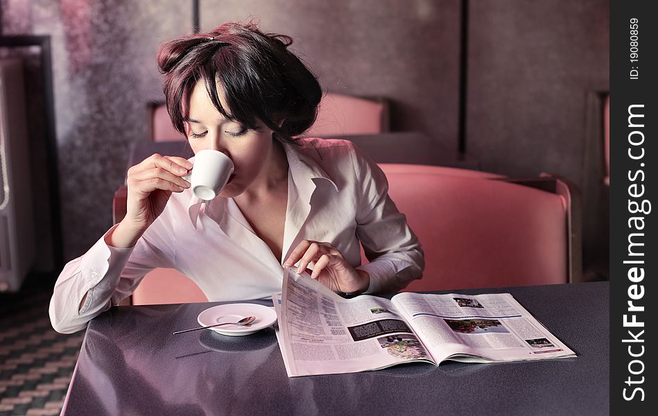 Young woman having breakfast while reading a newspaper in a bar