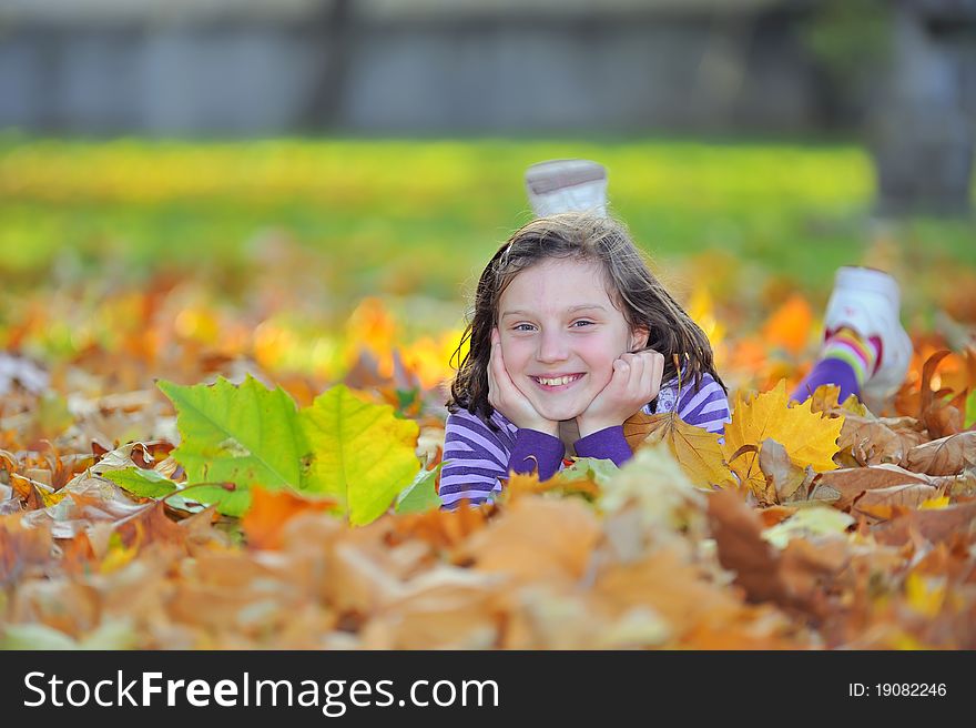 Smiling little girl laying on autumn leaves