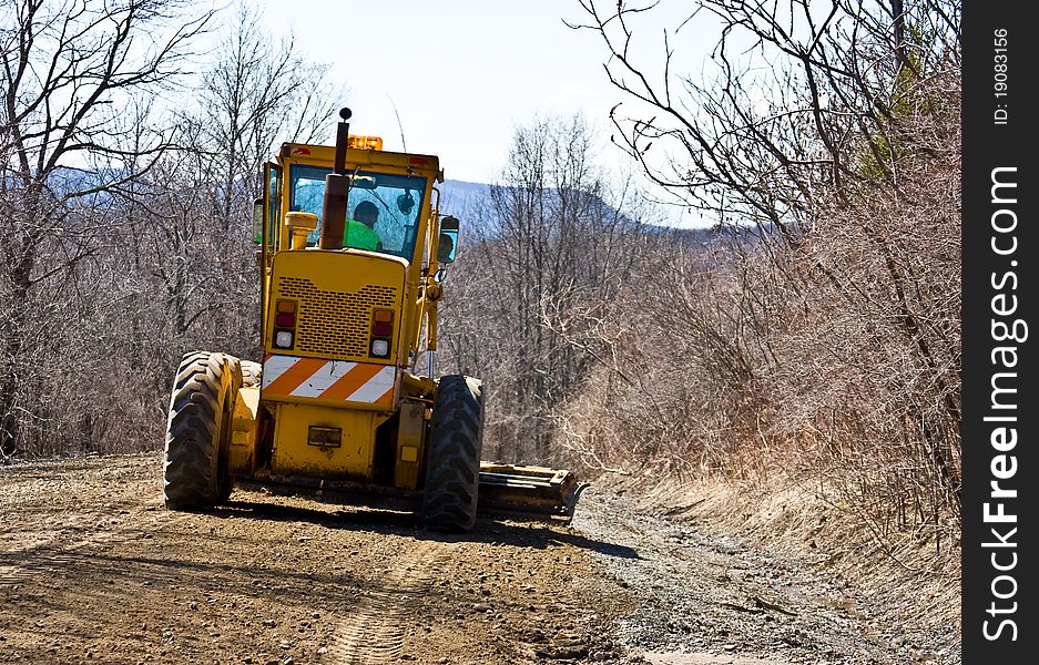 Road grader hard at work grading a back country dirt road.