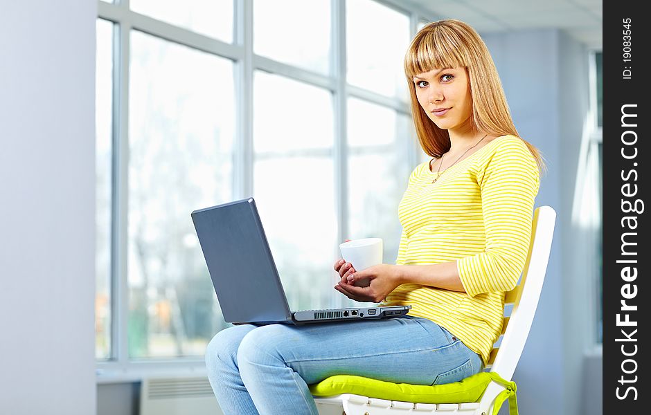 Casual girl sitting on the chair with notebook and holding a cup. Casual girl sitting on the chair with notebook and holding a cup