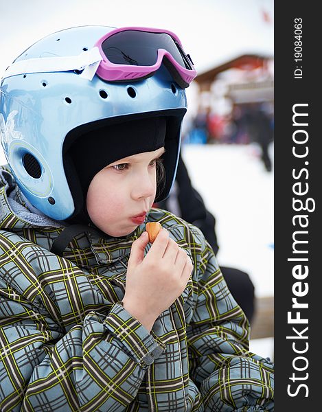Little girl in ski helmet and jacket eats sausage. Little girl in ski helmet and jacket eats sausage