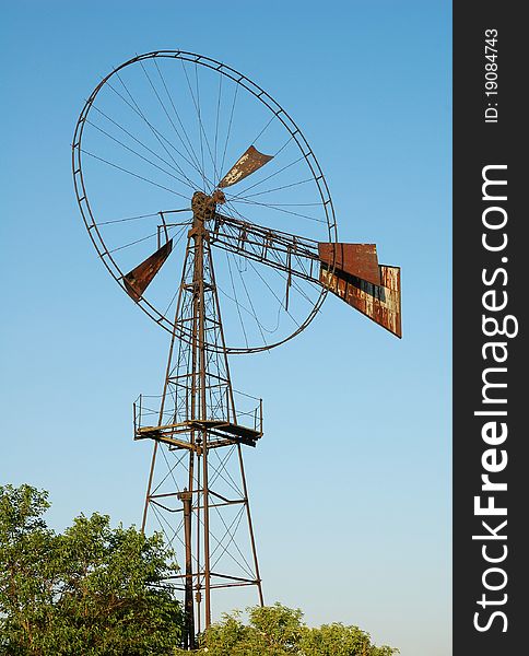 Old rusted windmill over green trees. Old rusted windmill over green trees