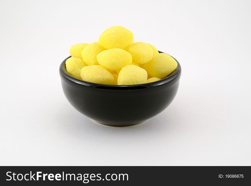 Many yellow lemon drops in a small black bowl on white background. Many yellow lemon drops in a small black bowl on white background