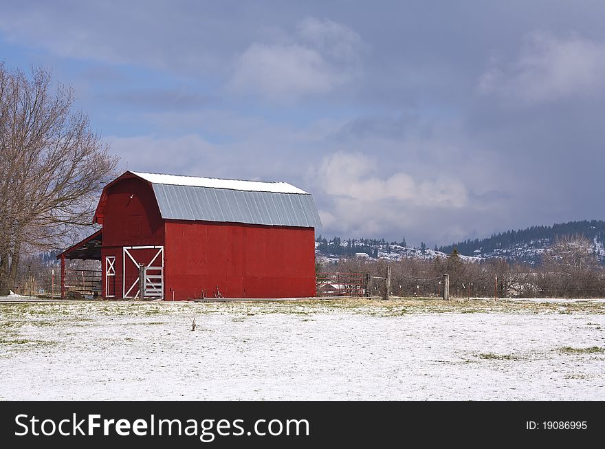A bright red barn against a cloudy blue sky with a light layer of snow in spring. A bright red barn against a cloudy blue sky with a light layer of snow in spring.