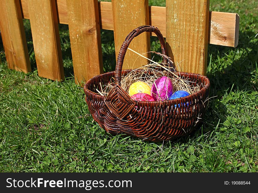 Some coloured easter eggs lying in a basket in front of a wooden fence