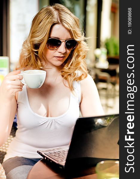 Blonde Woman sitting in a Cafe, looking into her Laptop with Cup in her Hand. Blonde Woman sitting in a Cafe, looking into her Laptop with Cup in her Hand