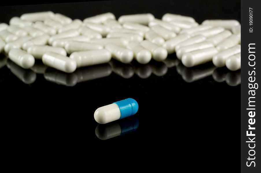 White-and-blue pill in front of white ones on black reflective background. White-and-blue pill in front of white ones on black reflective background