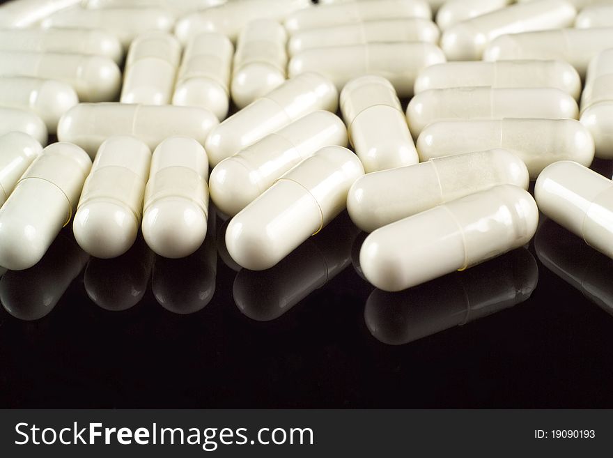 White pills (capsules) close-up on black reflective background. White pills (capsules) close-up on black reflective background