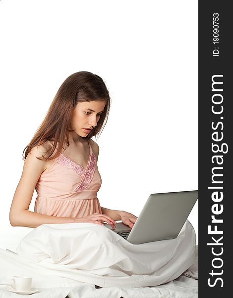 Young woman sitting in the bed and looking in laptop on a white background. Young woman sitting in the bed and looking in laptop on a white background