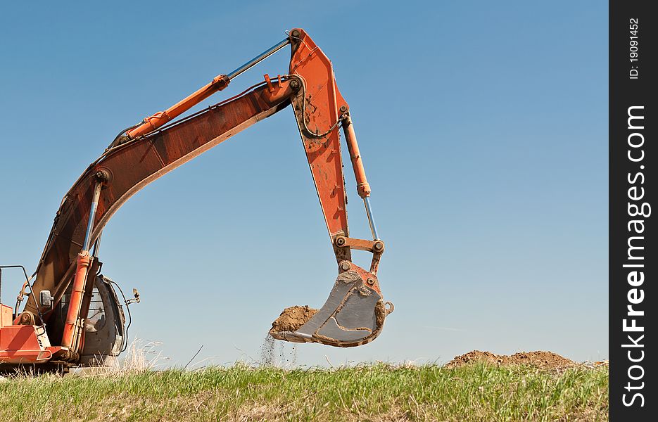 The arm and bucket of a hydraulic excavator that is digging into a grassy hillside. The arm and bucket of a hydraulic excavator that is digging into a grassy hillside.