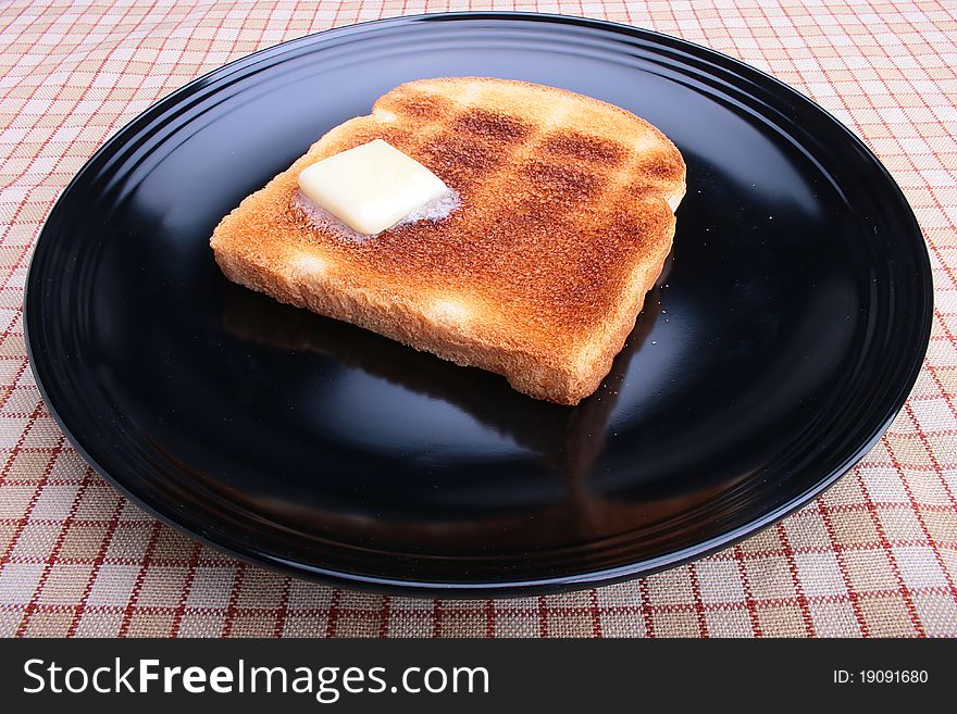 Toasted white bread with butter on a black plate. Toasted white bread with butter on a black plate.
