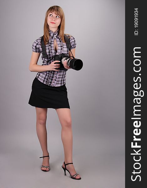 The young beautiful girl dressed in a short skirt and a blouse, has control over a modern camera. The young beautiful girl dressed in a short skirt and a blouse, has control over a modern camera