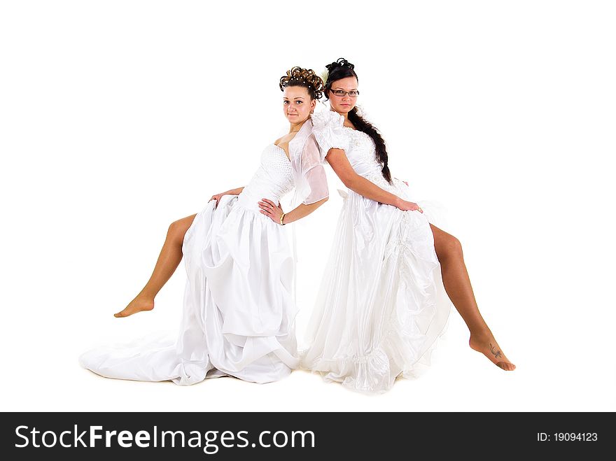 Two young beautiful brides is showing off their legs in wedding dress on white isolated background. Two young beautiful brides is showing off their legs in wedding dress on white isolated background.