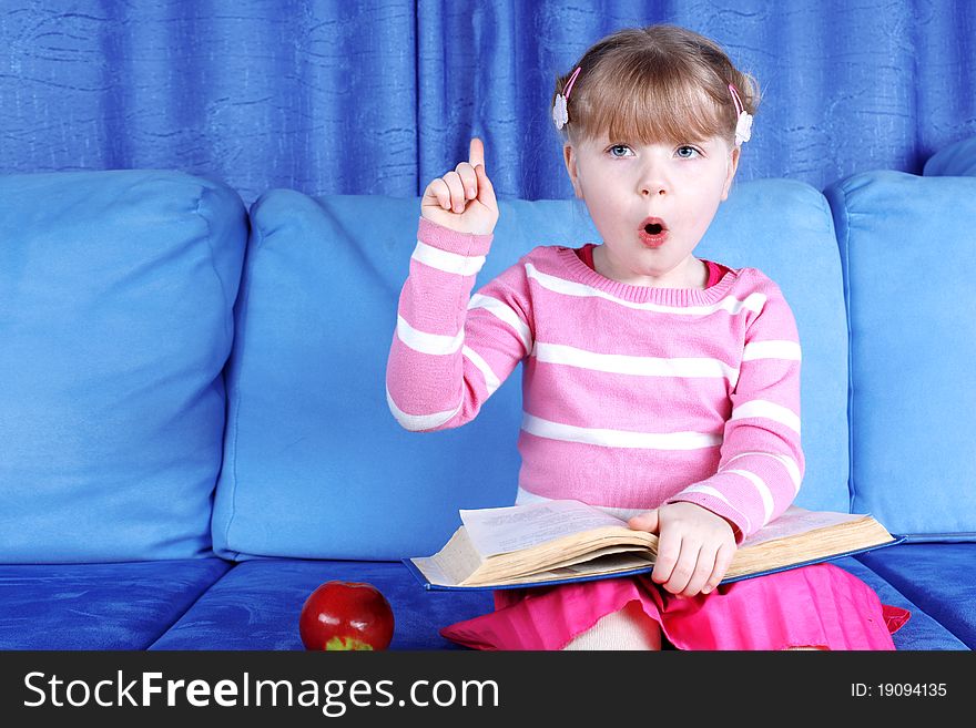 Surprised little girl with apple and books in sofa