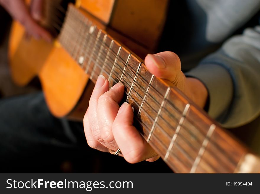 Brown guitar in hands of the guy playing it. Shallow depth of filed