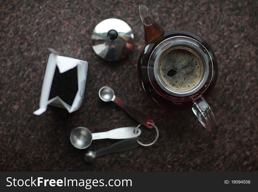 Bag of tea leaves, measuring spoons and teapot full of water and tea on a granite countertop, viewed from above. Bag of tea leaves, measuring spoons and teapot full of water and tea on a granite countertop, viewed from above