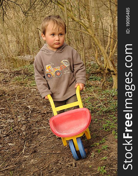 Little boy with an empty  wheelbarrow working in a desolate garden. Little boy with an empty  wheelbarrow working in a desolate garden