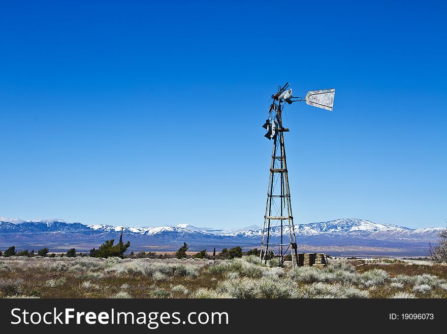 A long-abandoned windmill stands on windswept desert farm against big blue sky. A long-abandoned windmill stands on windswept desert farm against big blue sky.