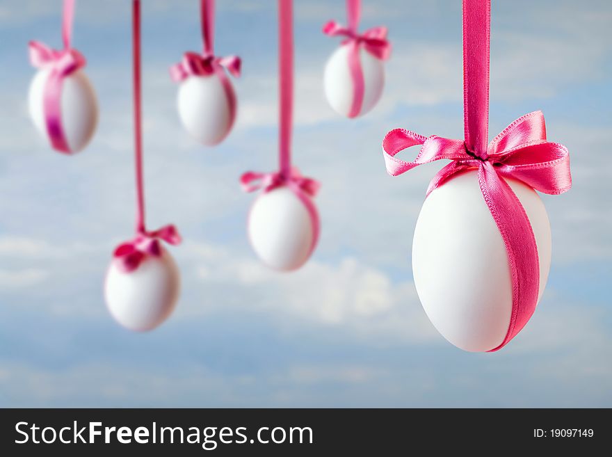 Six white easter eggs hanged on the pink satin ribbons on the blue sky background. Six white easter eggs hanged on the pink satin ribbons on the blue sky background