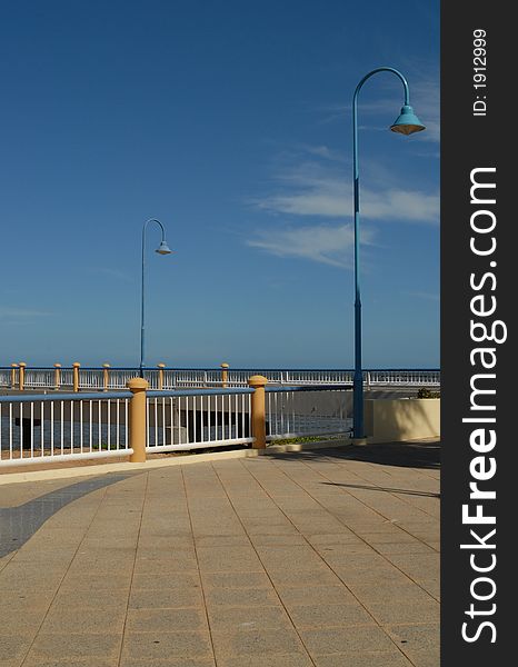 Paving, bollards and lamp post with pier in background, blue sky. Paving, bollards and lamp post with pier in background, blue sky