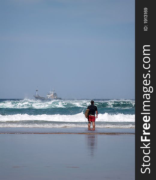 A surfer watching the waves and a ship in the background