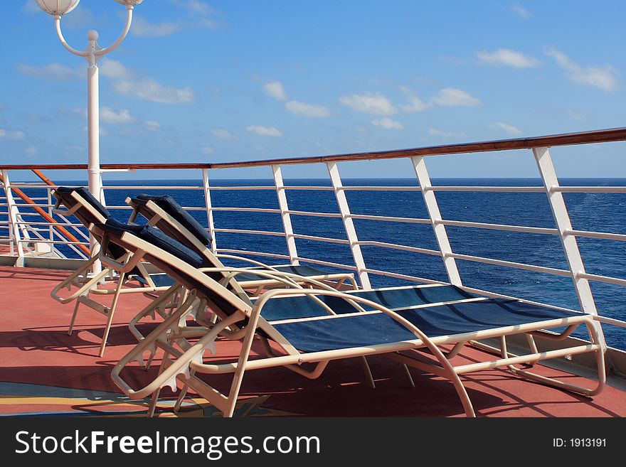 Lounge chairs overlooking the blue ocean behind the railing on a vacation cruise ship. Lounge chairs overlooking the blue ocean behind the railing on a vacation cruise ship.