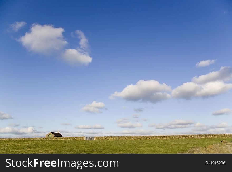 A lonely house on a stretch of green grass under a blue sky with white couds. A lonely house on a stretch of green grass under a blue sky with white couds.