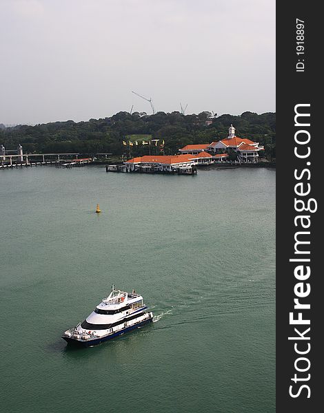 A ferry moving on sea. Background is Sentosa island, a tourism spot in Singapore.