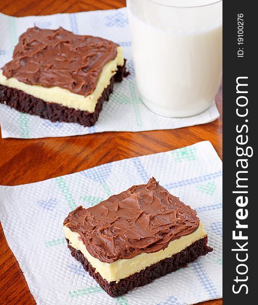 Fudge cheesecake brownie with chocolate icing on a napkin and a glass of milk