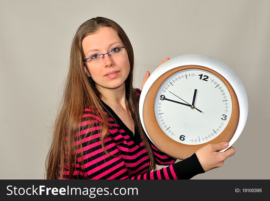 A young girl holding a wall clock against a gray background. A young girl holding a wall clock against a gray background