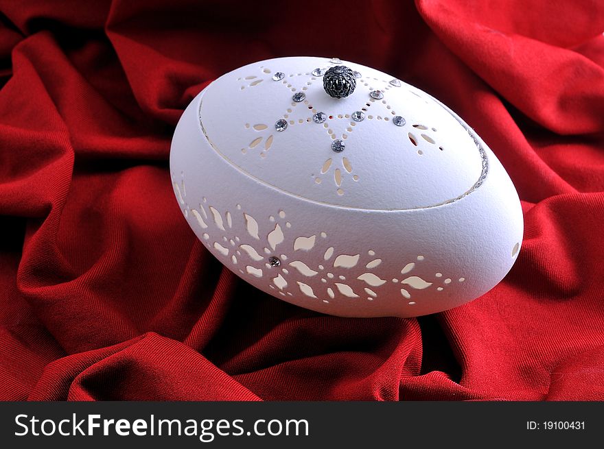 Decorative casket from a goose egg rests against a red background
