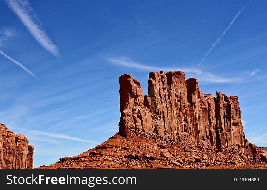 Jagged lines of a red rock mountain from Monument Valley, Arizona, reach up to a blue sky.