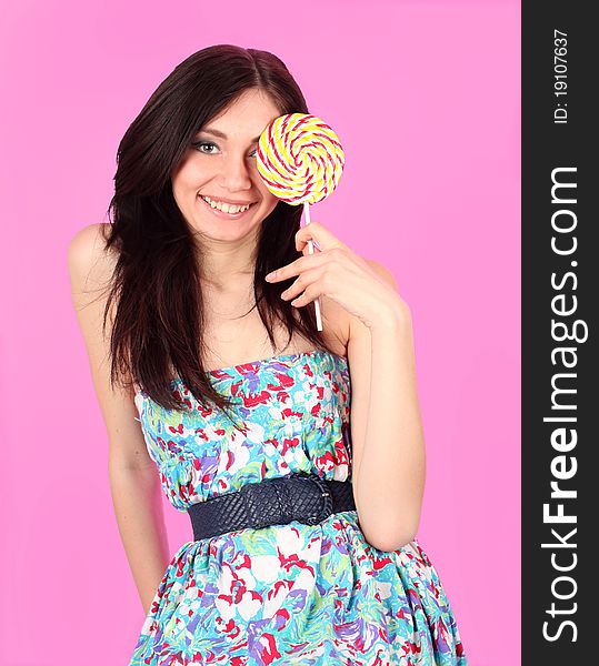 Portrait of glamorous cheerful girl wearing colorful dress with lollipop over pink background. Portrait of glamorous cheerful girl wearing colorful dress with lollipop over pink background