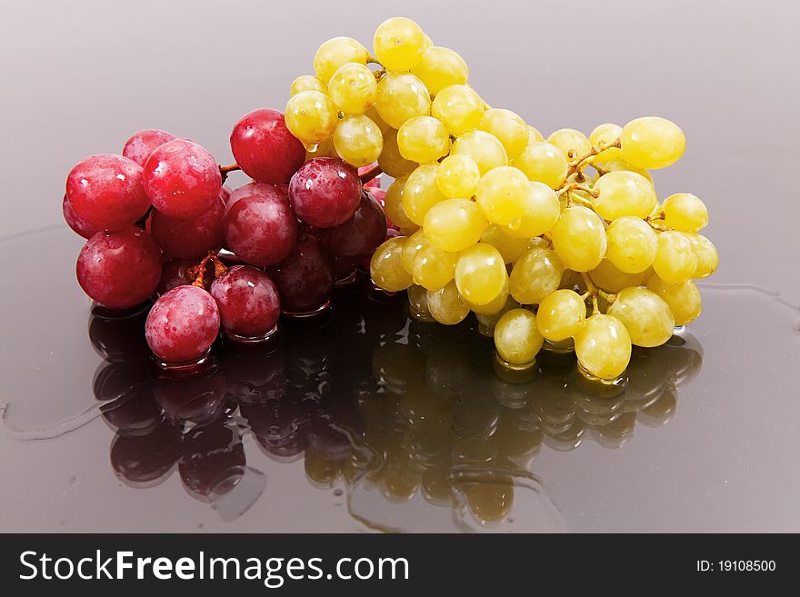 Cluster of red large and green grapes against a dark background with reflexion on water