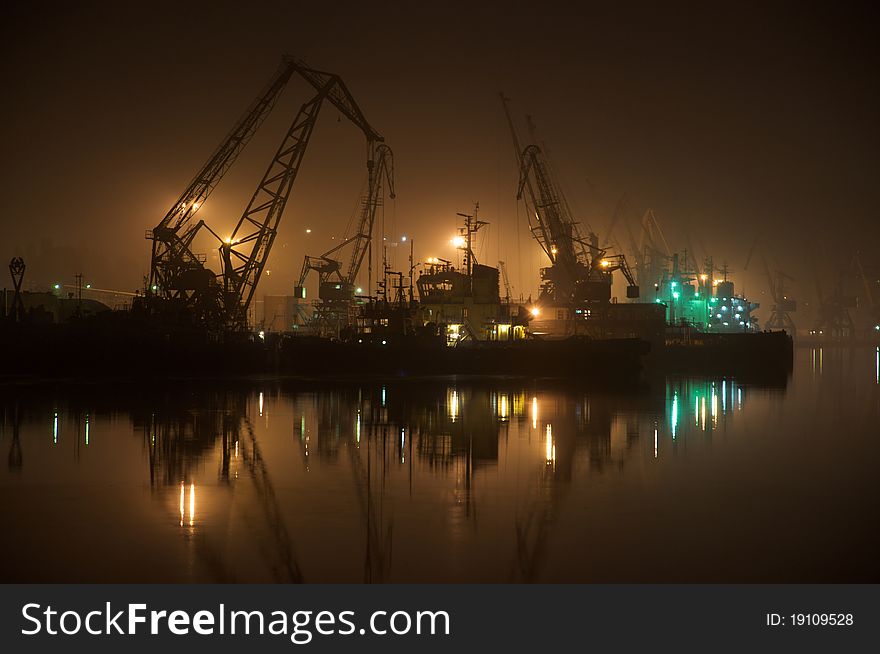 Ships and cranes at night in the calm port over water reflections. Ships and cranes at night in the calm port over water reflections.