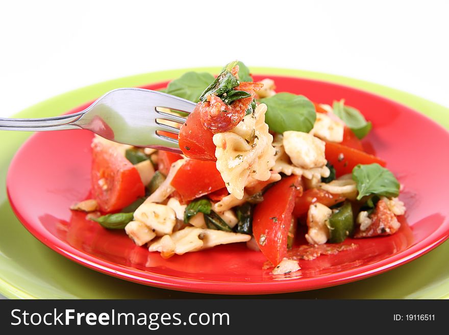 Salad - made of farfalle pasta, tomato, salami, bell pepper and mozzarella, decorated with basil, being eaten with a fork