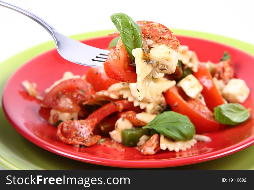 Salad - made of farfalle pasta, tomato, salami, bell pepper and mozzarella, decorated with basil, being eaten with a fork