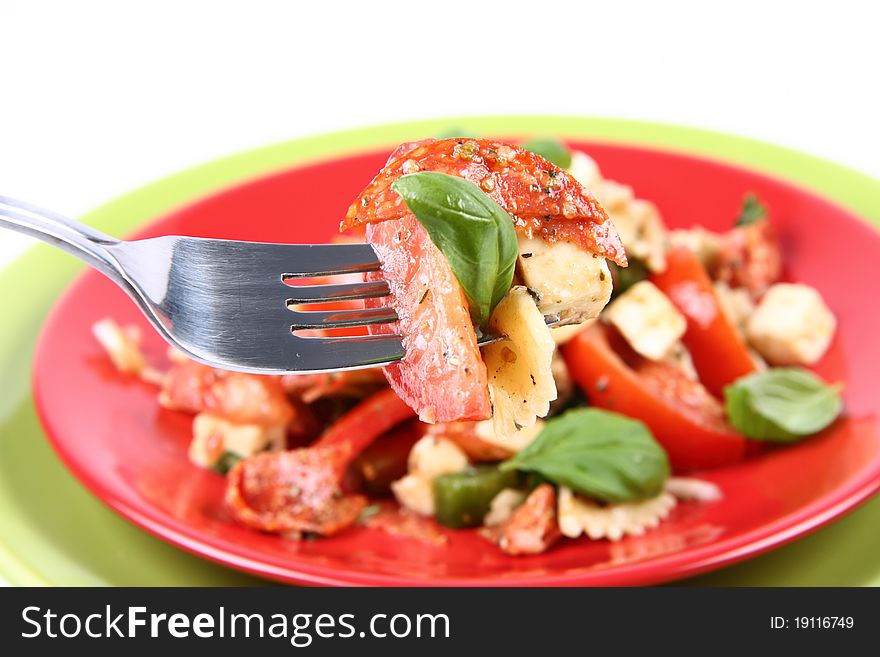 Salad - made of farfalle pasta, tomato, salami, bell pepper and mozzarella, decorated with basil, being eaten with a fork