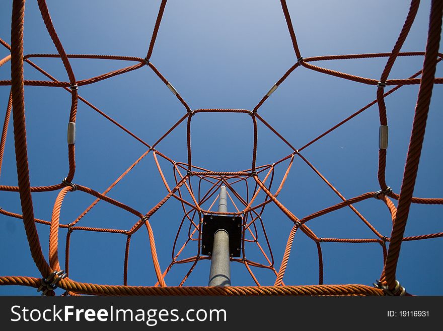 A spatial playground climbing net made of red plastic rope and steel pipe photographed against blue sky. A spatial playground climbing net made of red plastic rope and steel pipe photographed against blue sky.