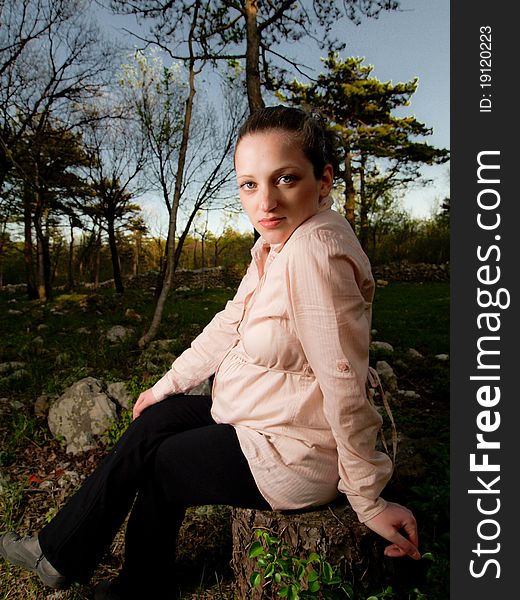 Pregnancy in nature, beautiful young and pregnant women in forest sitting on stump