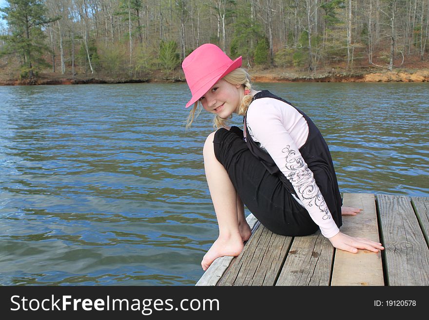 Young girl in a pink hat sitting on the edge of a dock. Young girl in a pink hat sitting on the edge of a dock.