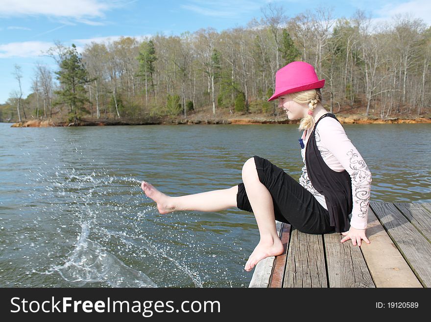 Young girl in a pink hats splashing water from the lake with her foot. Young girl in a pink hats splashing water from the lake with her foot.