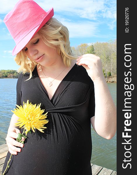 Pregnant woman in a natural setting wearing a pink hat and holding a flower. Pregnant woman in a natural setting wearing a pink hat and holding a flower.