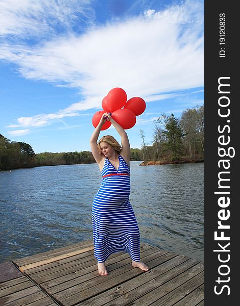 Pregnant woman on a dock holding a bunch of red balloons above her head. Pregnant woman on a dock holding a bunch of red balloons above her head.