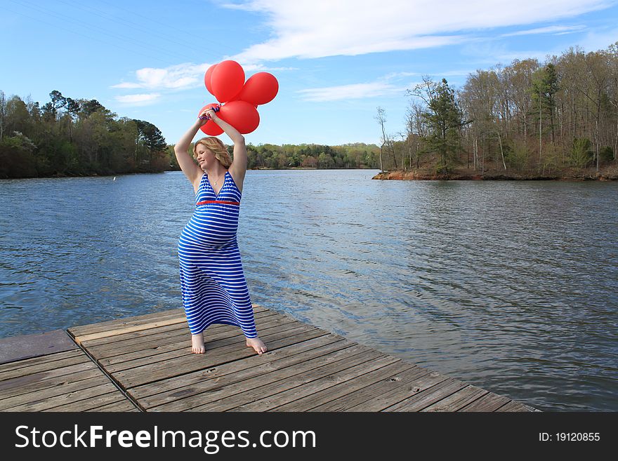 Beautiful happy pregnant woman holding balloons on the dock in a beautiful natural setting. Beautiful happy pregnant woman holding balloons on the dock in a beautiful natural setting.