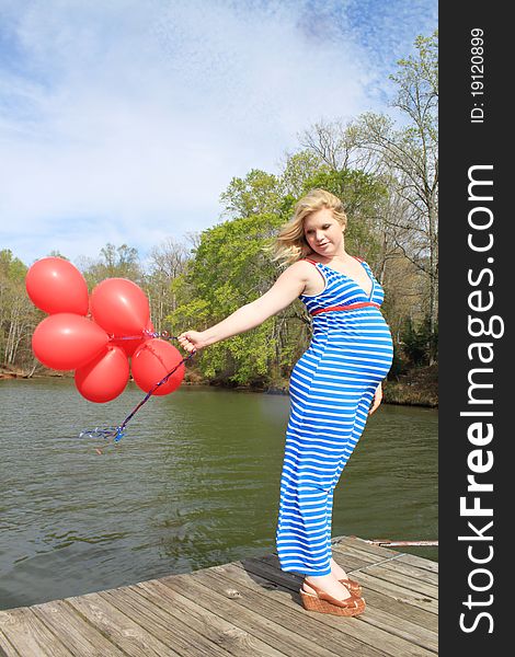 Beautiful pregnant woman with red ballons on a dock in a natural setting. Beautiful pregnant woman with red ballons on a dock in a natural setting.