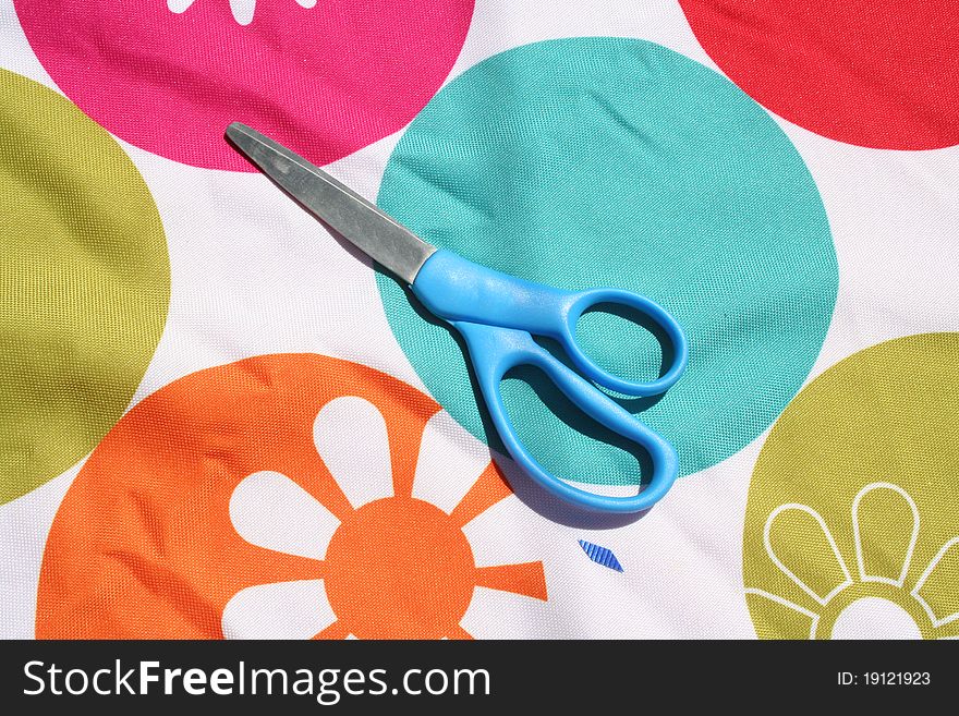 Scissors sitting on a colorful table cloth.