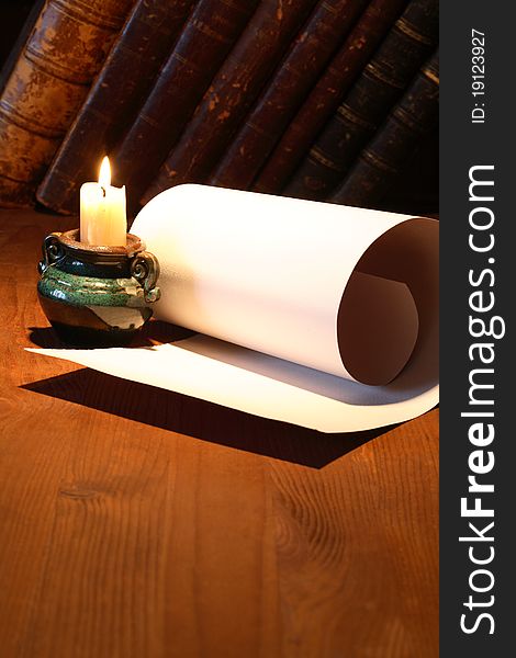 Old paper near lighting candle and stack of vintage books on wooden surface. Old paper near lighting candle and stack of vintage books on wooden surface